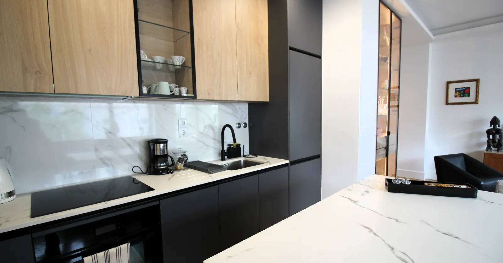 Cozinha moderna de pequena dimensão com armários em madeira e preto mate, bancada em mármore branco e eletrodomésticos integrados — exemplo de aproveitamento elegante e funcional de espaços reduzidos.
