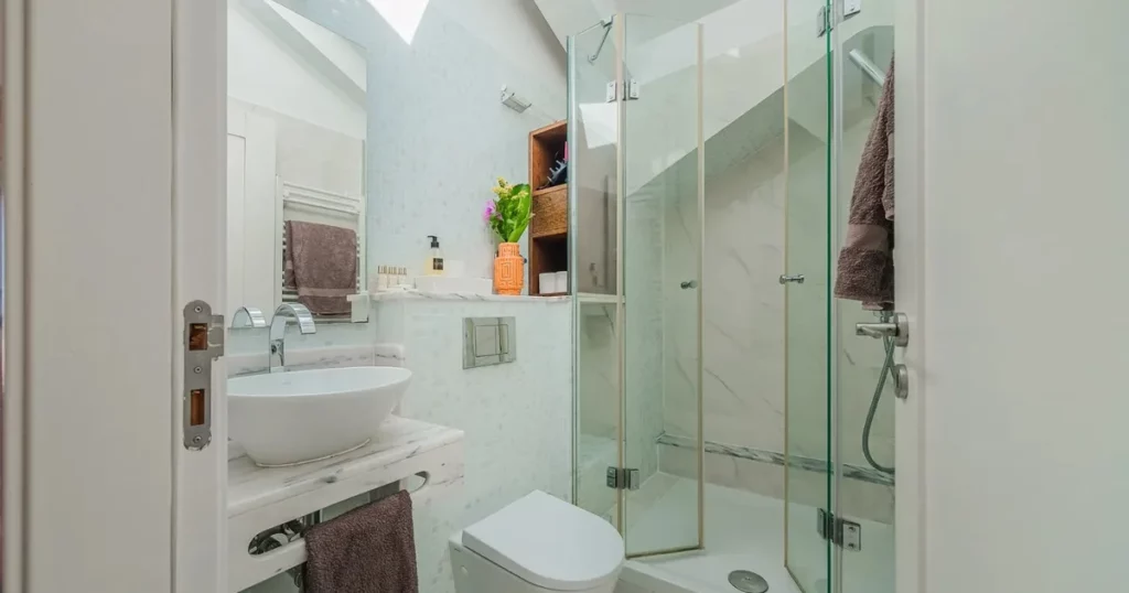 Casa de banho compacta com lavatório em mármore, espelho integrado e box de duche em vidro com luz natural